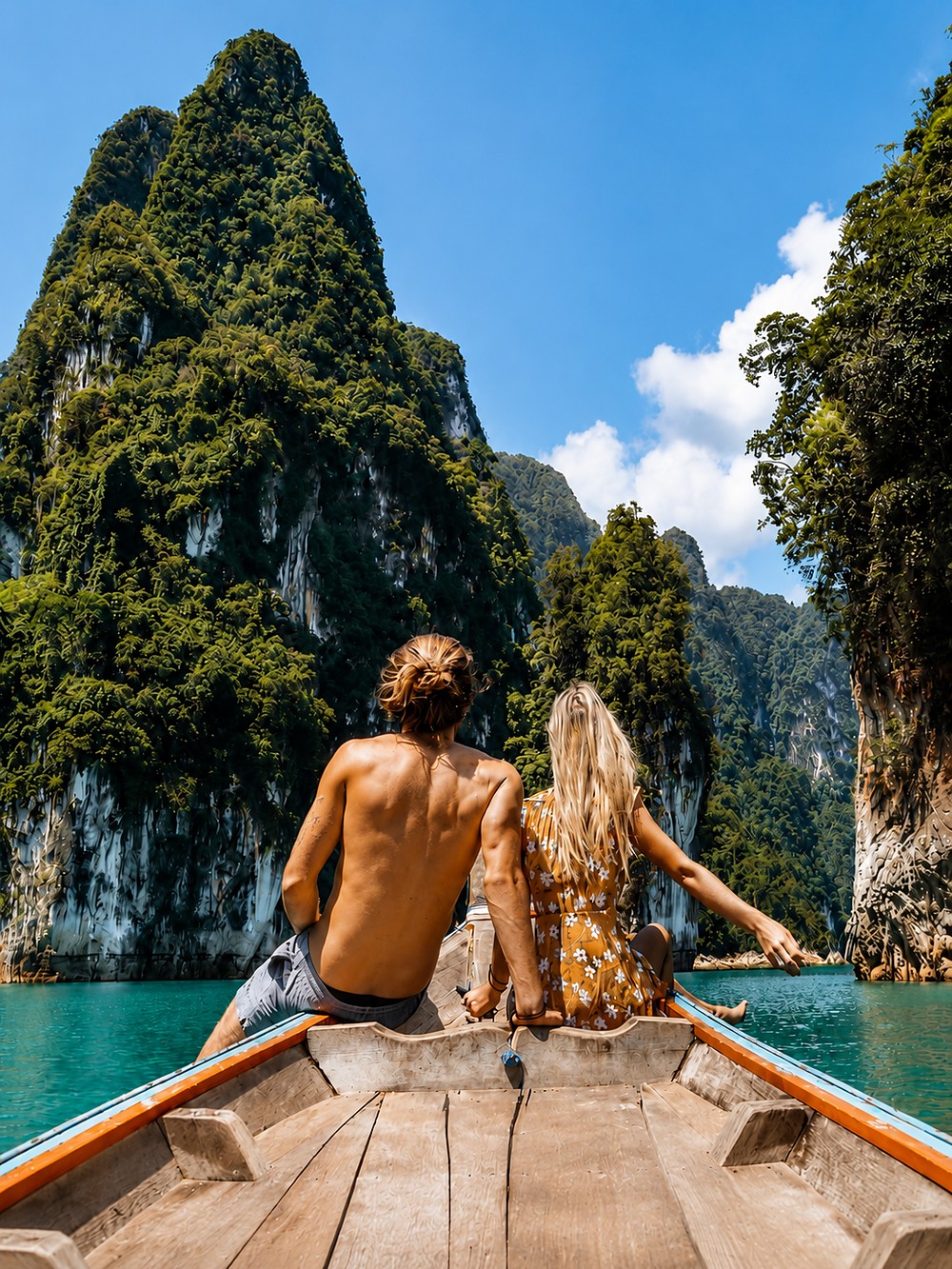 Casal observando as montanhas calcárias do Lago Cheow Lan a bordo de um barco tradicional, na Tailândia