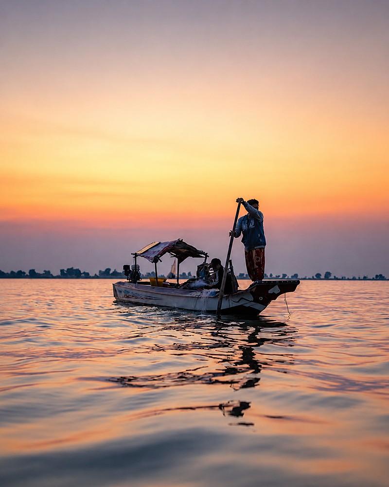 Pescador conduzindo um barco ao entardecer em um lago no Camboja