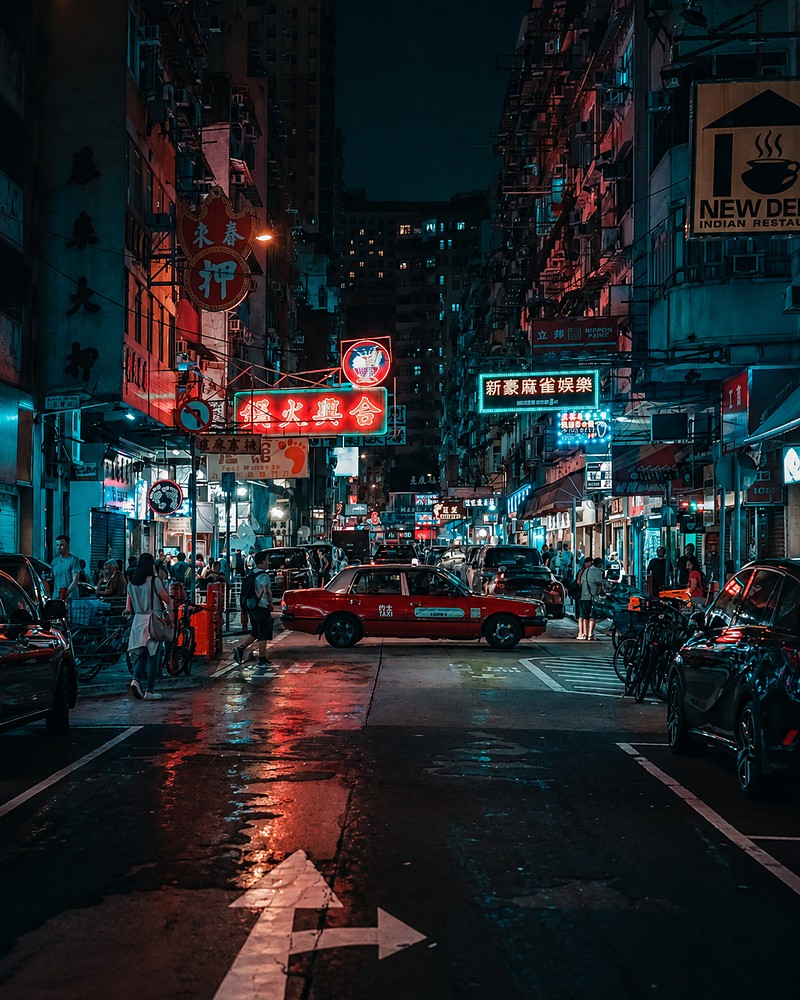 Rua movimentada à noite, com letreiros neon e táxi vermelho em Hong Kong