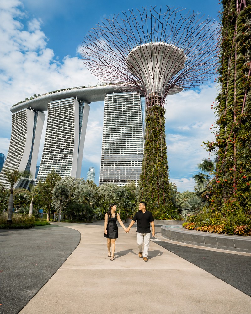 Casal caminhando de mãos dadas nos Jardins da Baía, com o Marina Bay Sands e os Supertrees ao fundo, em Singapura